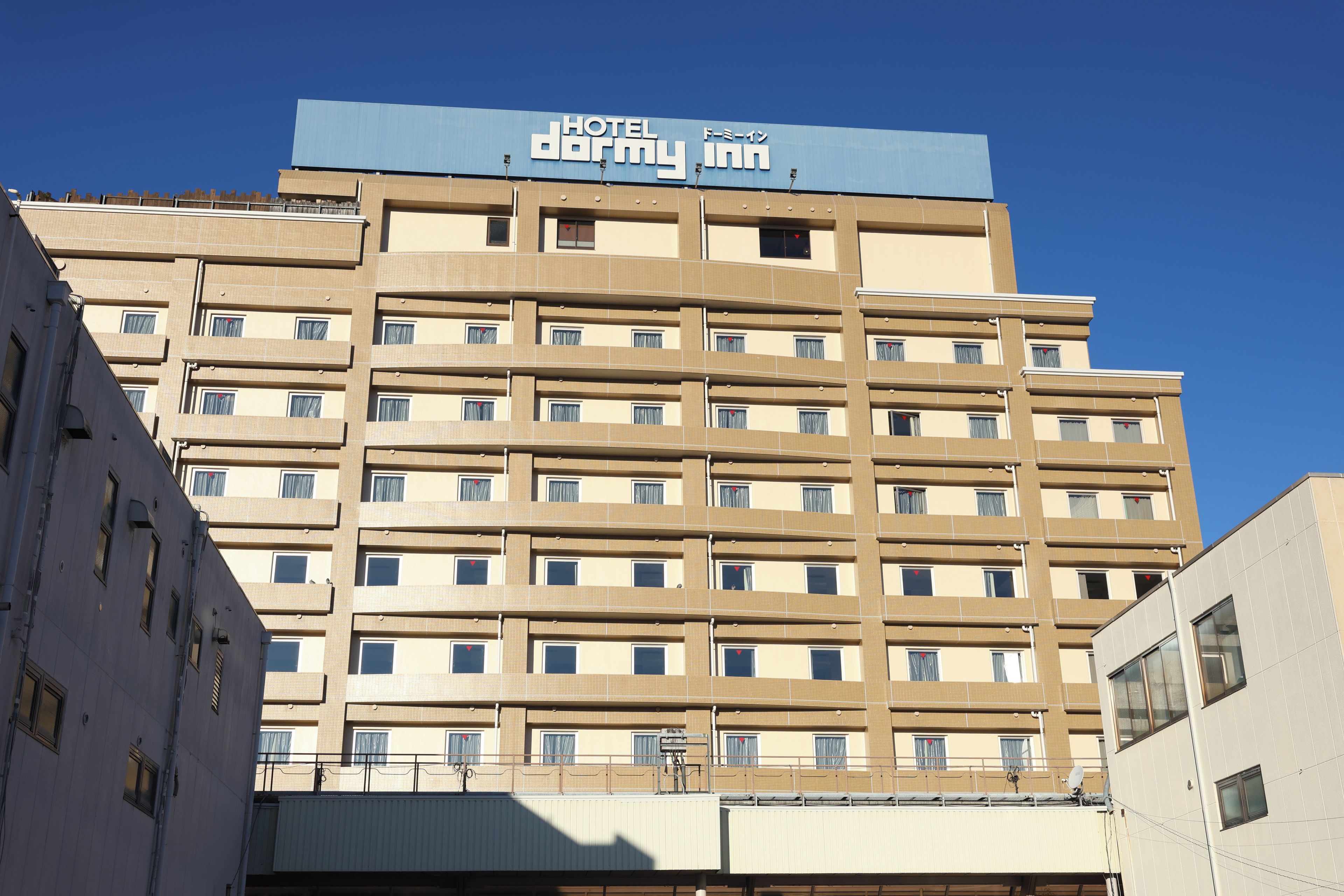 Un immeuble hôtelier à plusieurs étages, surmonté d’une enseigne bien visible indiquant « HOTEL dormy inn ».