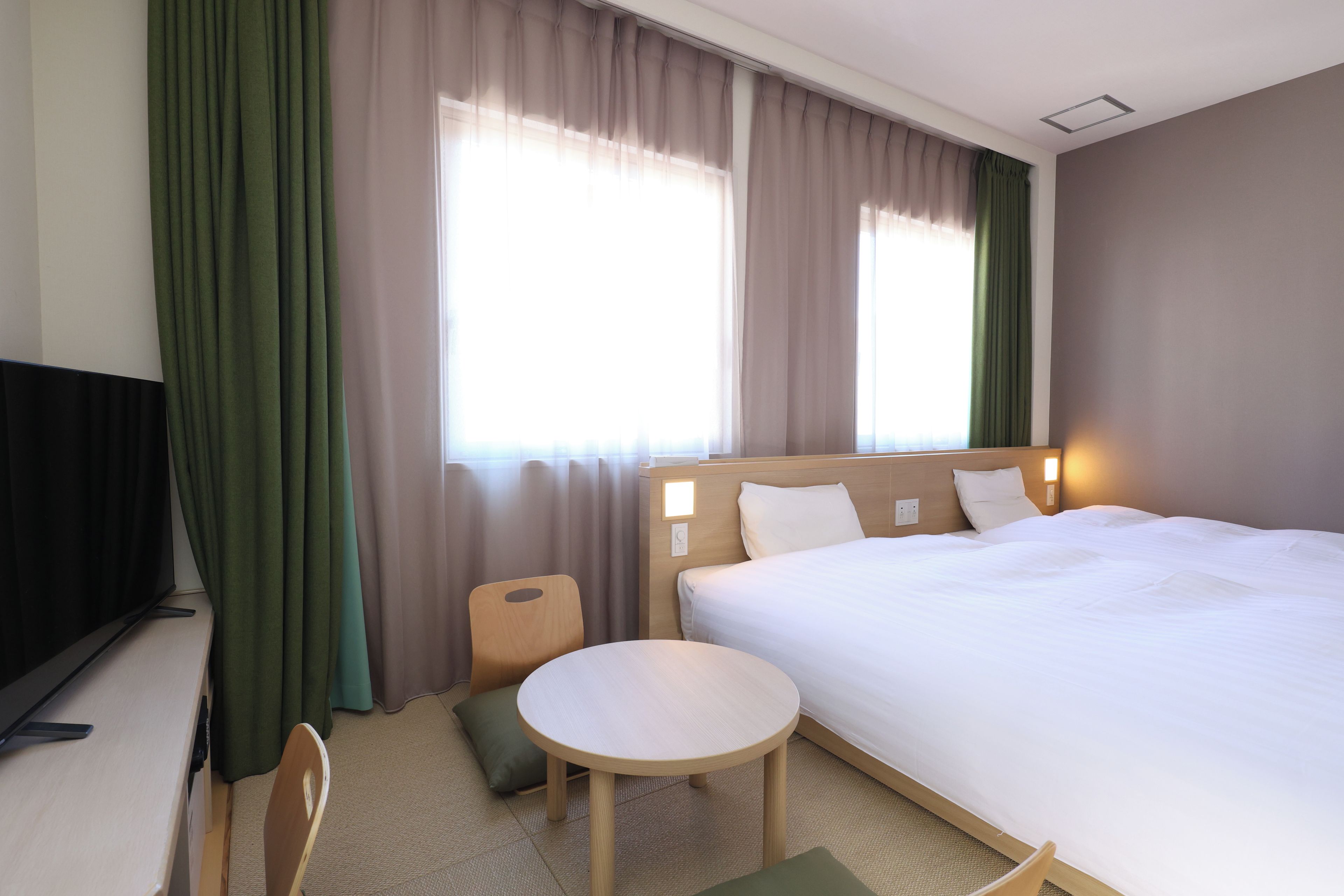 A hotel room with a bed, a small table, a chair, a TV, and curtains.