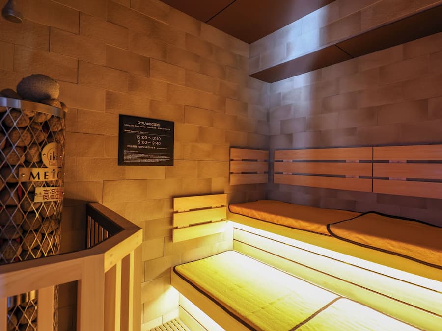 A sauna with a wooden bench and a wall-mounted sign with operating hours.