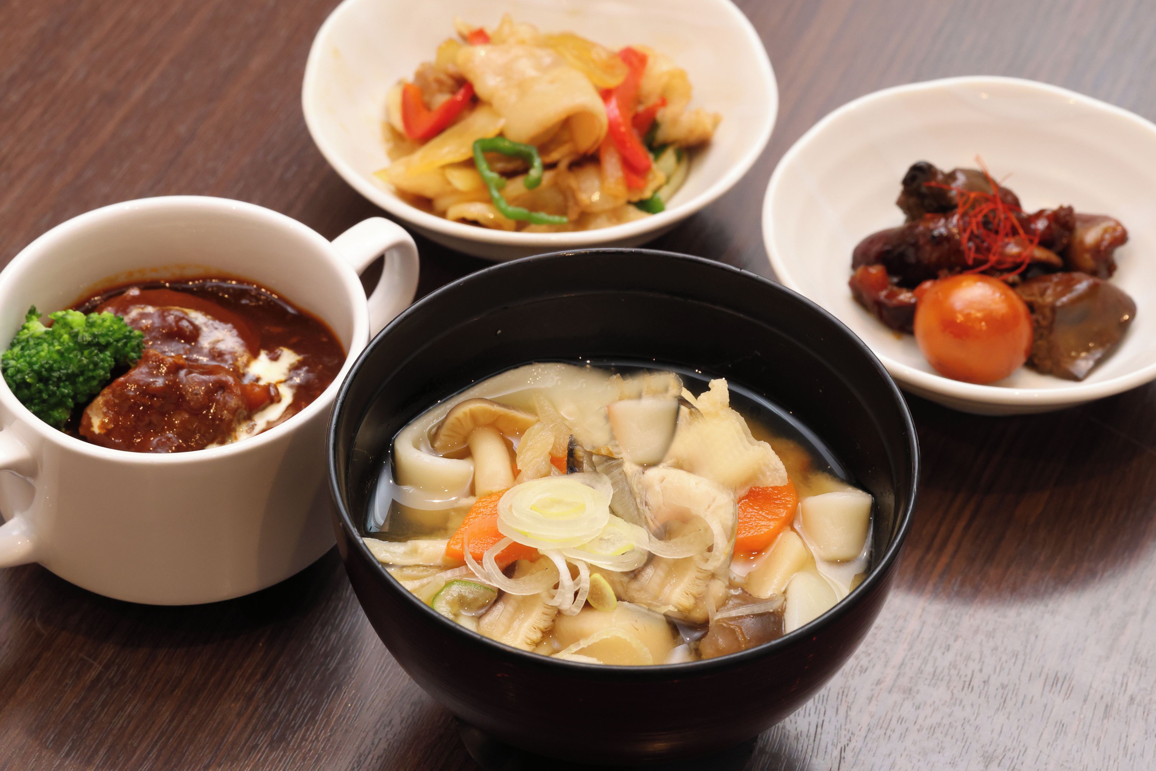 A table with four bowls of food, one of which is a clear broth with vegetables.