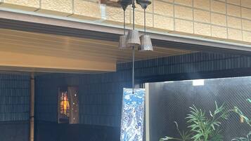 A room with a tiled ceiling, a hanging light fixture, a window with a patterned view, and a plant.