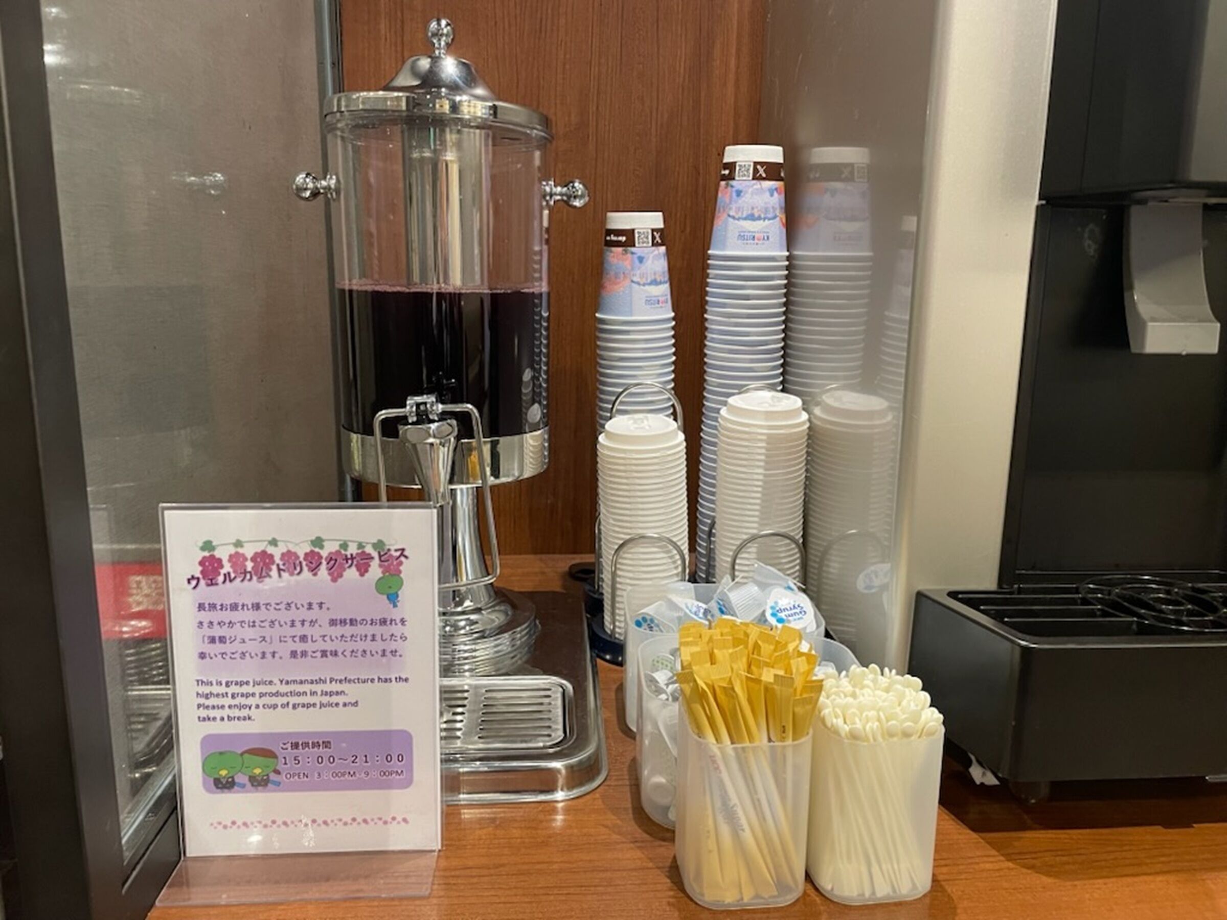 A beverage station with a glass carafe, disposable cups, and utensils.