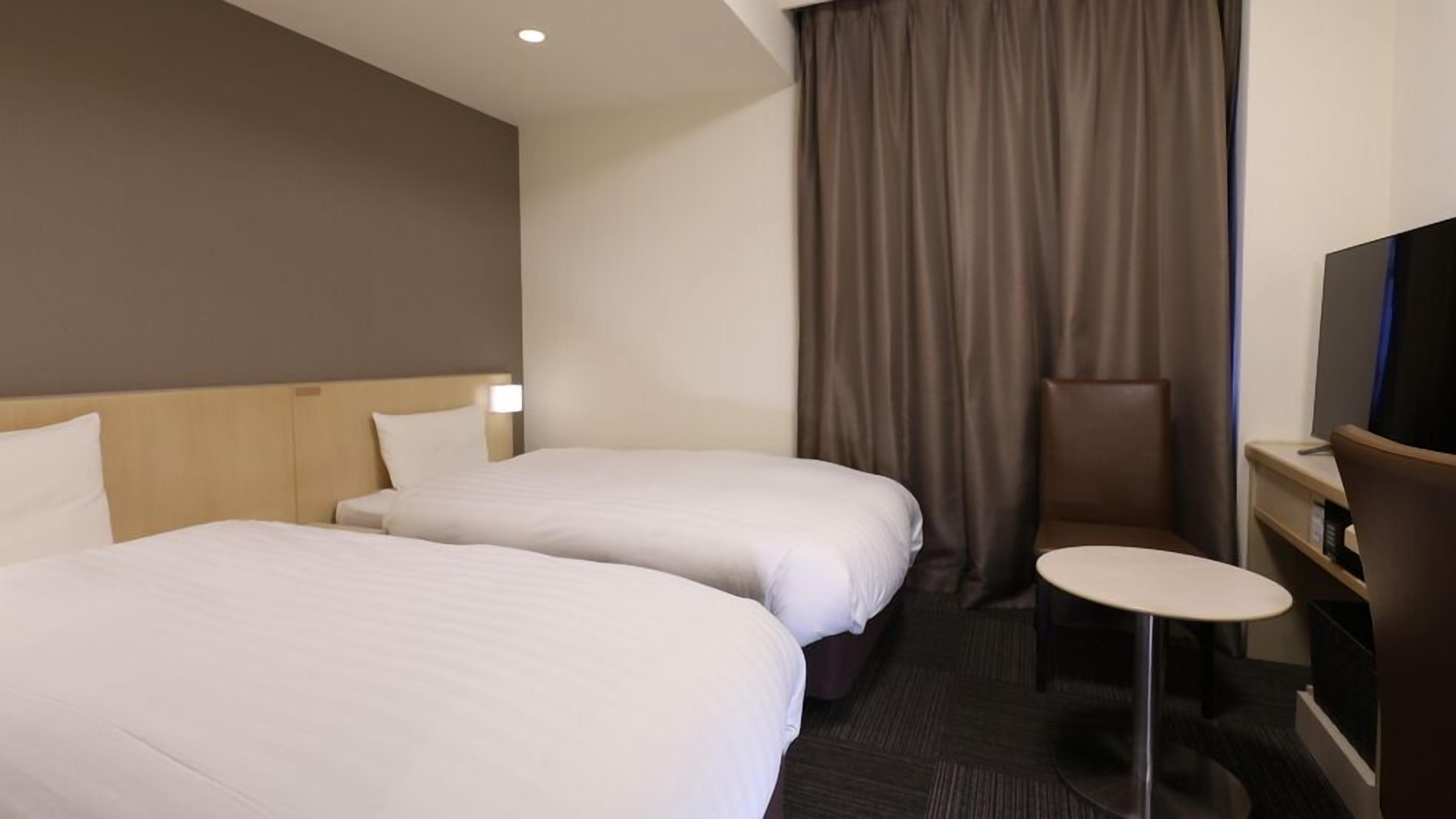 A hotel room with two beds, a small round table, a TV, and a curtain.