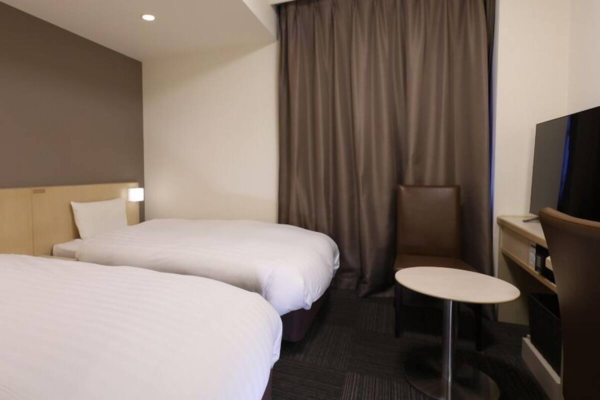 A hotel room with two beds, a small round table, a TV, and a curtain.