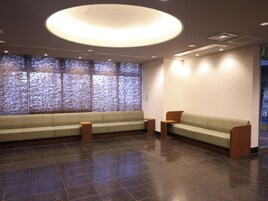 A modern waiting area with a large, circular ceiling light, a long bench, and a wall with a textured pattern.