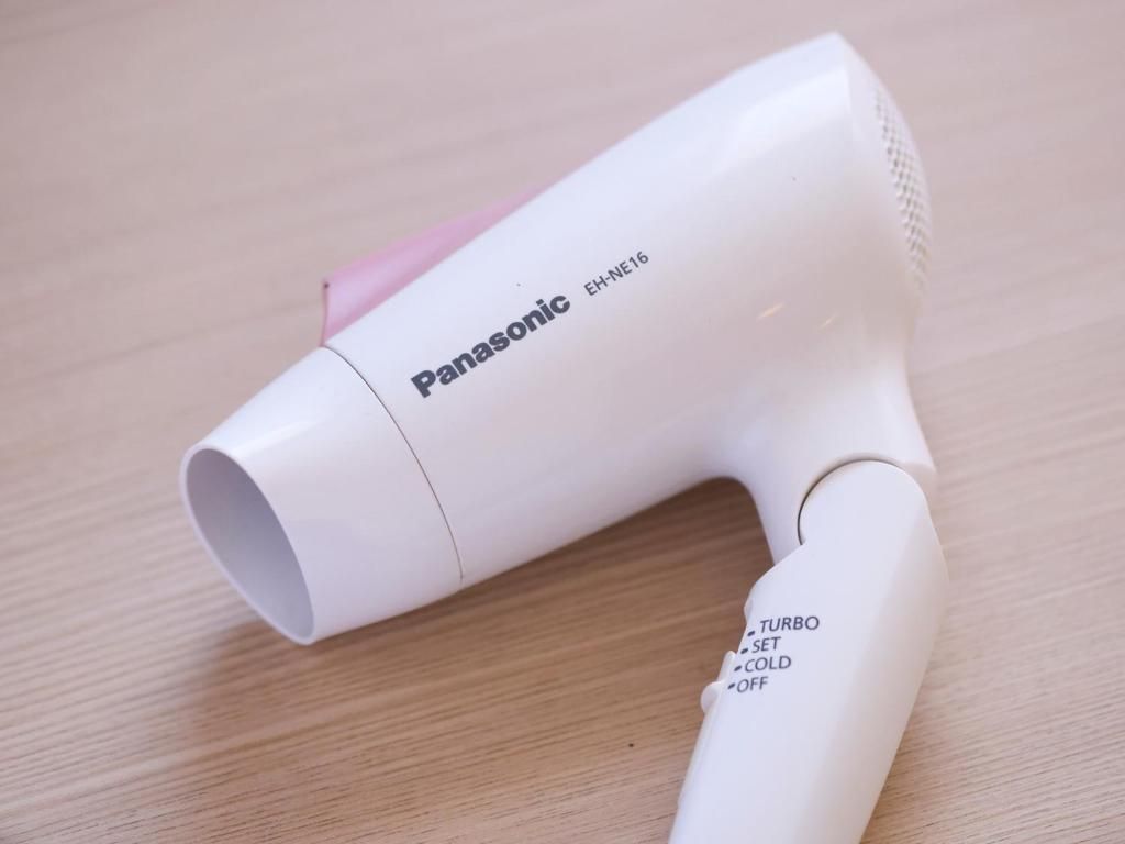 A Panasonic hair dryer with a white body and a pink accent, placed on a wooden surface.