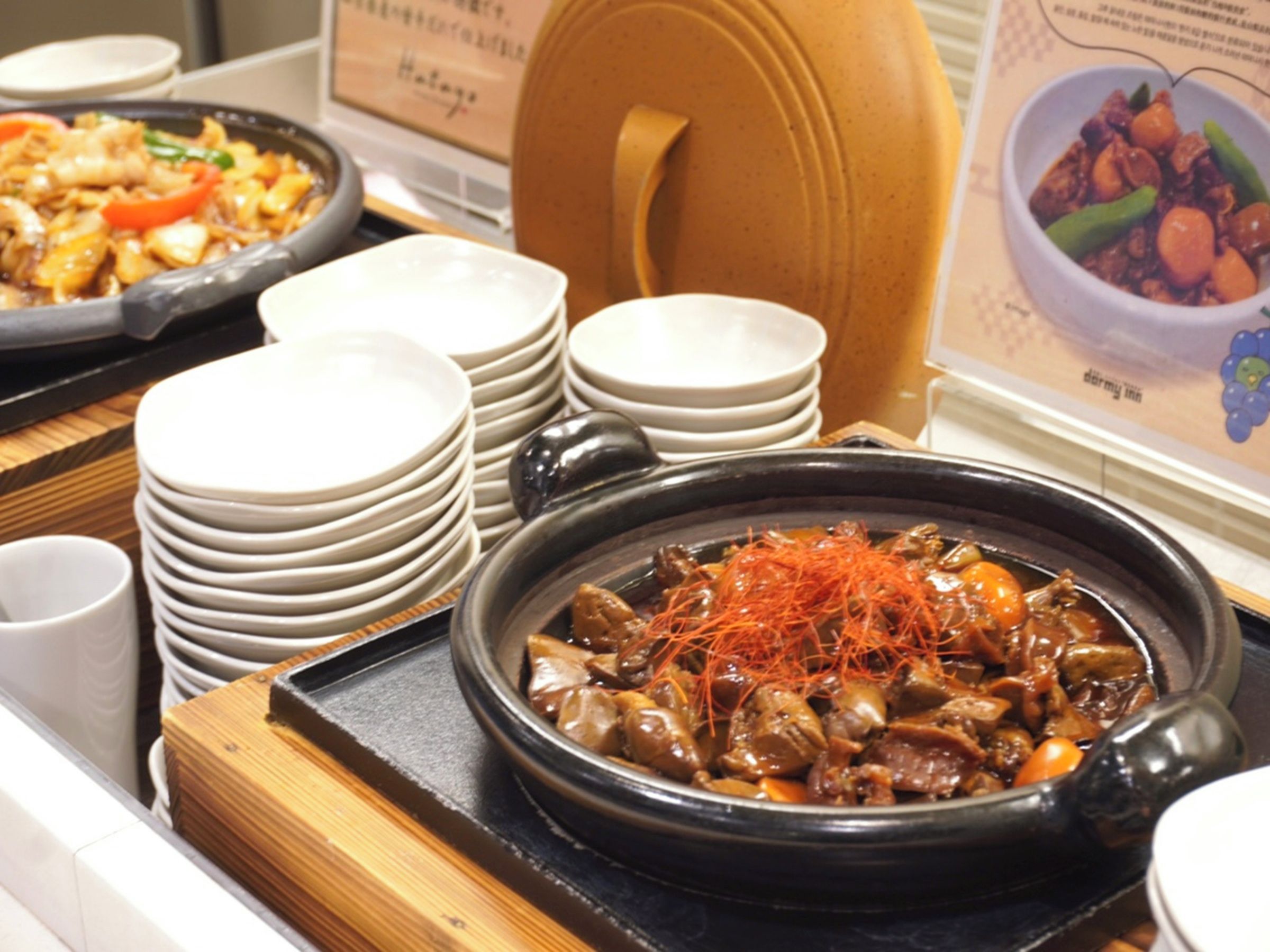 A dining area with multiple dishes, including a bowl of stew garnished with carrot strips, and a variety of plates and bowls stacked on a table.