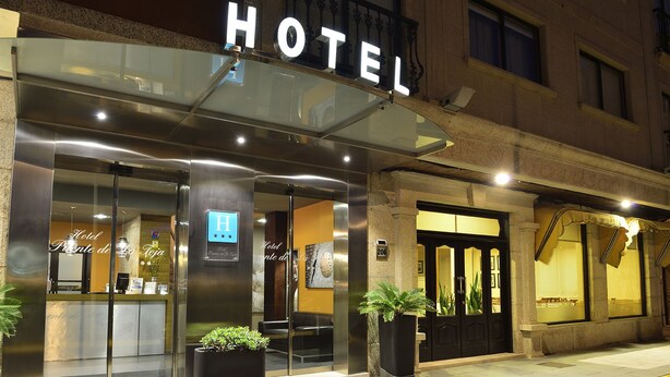 Entrada de hotel con fachada de vidrio, una recepción y un cartel con el nombre del hotel.