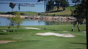 Un campo de golf con búnkeres, una masa de agua y árboles.