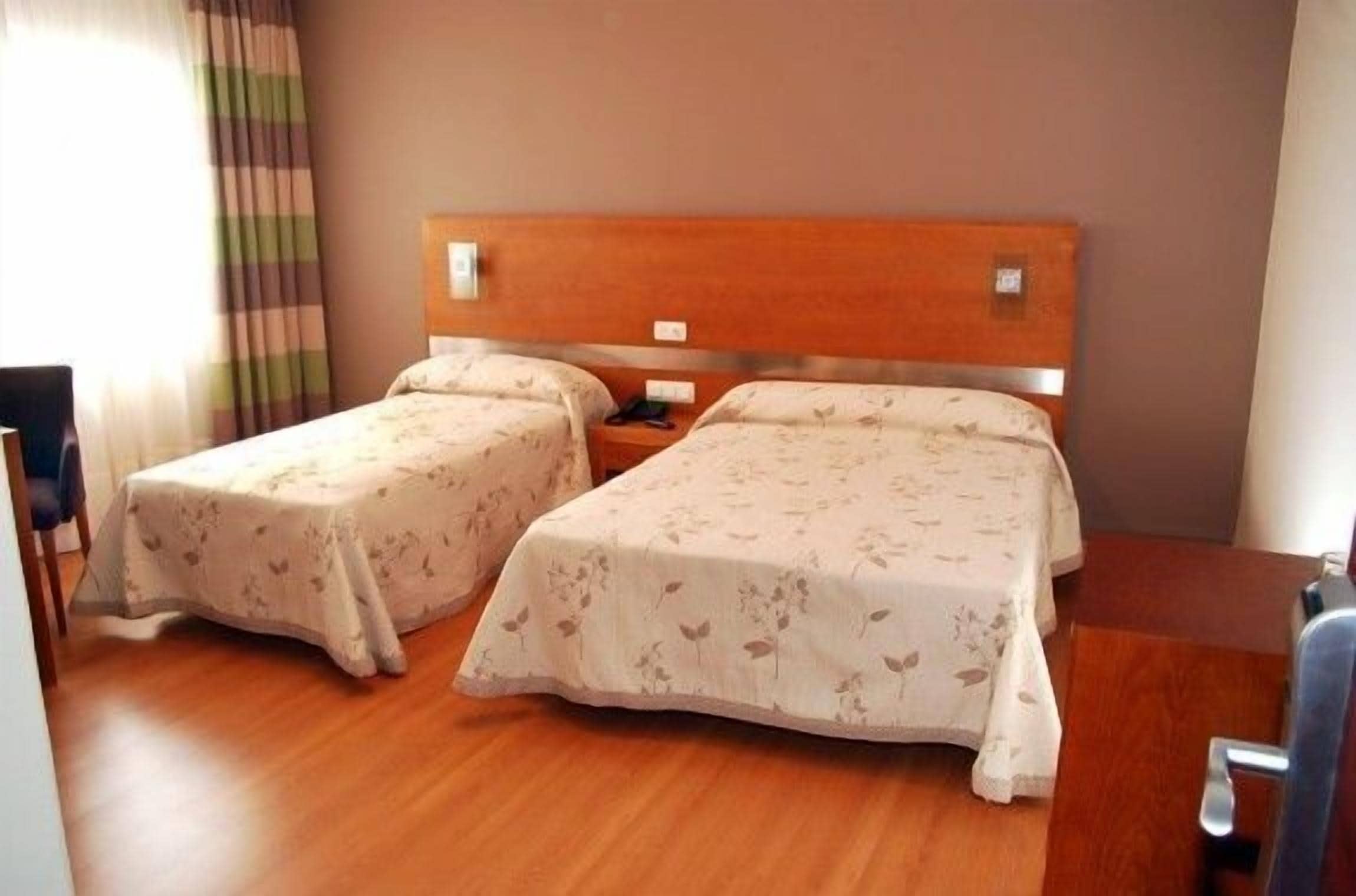 A hotel room with two single beds, wooden flooring, a wooden headboard, and a nightstand.