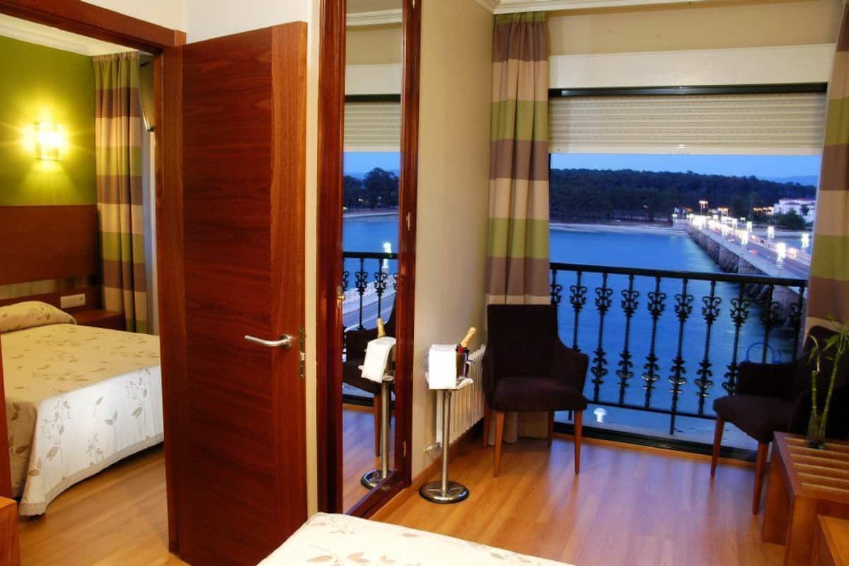 Ein Hotelzimmer mit Bett, Schreibtisch, Stuhl und Blick auf ein Gewässer mit einer Brücke.