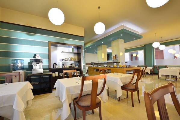 Un comedor con mesas y sillas, una barra de buffet y un dispensador de agua.
