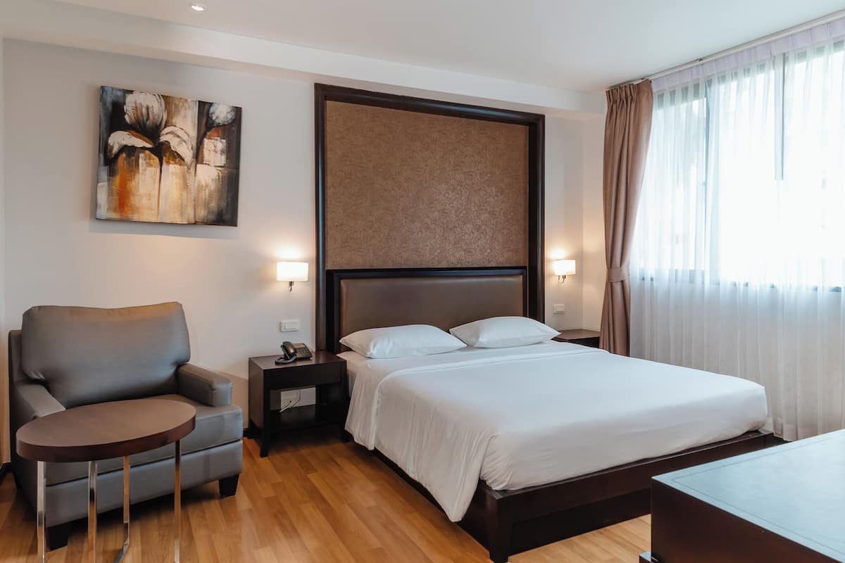 Een hotelkamer met een bed, een stoel, een klein tafeltje, een nachtkastje en een schilderij aan de muur.