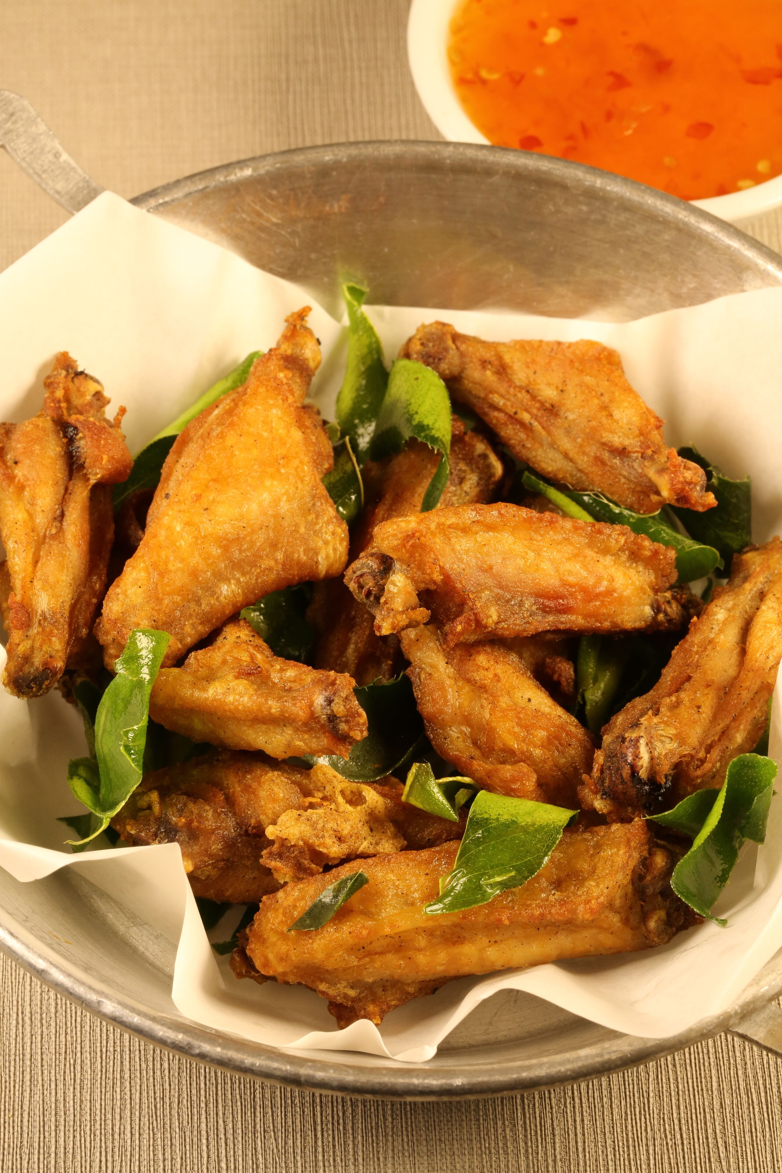 A bowl of fried chicken wings with greens and a side of sauce.