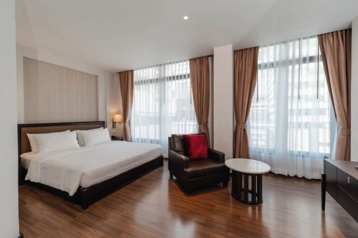A hotel room with a large bed, a leather armchair, a small round table, and a desk.