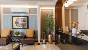 A modern hotel lobby with leather sofas, a reception desk, a large framed artwork, a potted plant, and a decorative vase.
