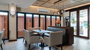A modern dining area with a table, chairs, and a booth. There is a clock on the wall and an air conditioning unit above the table.