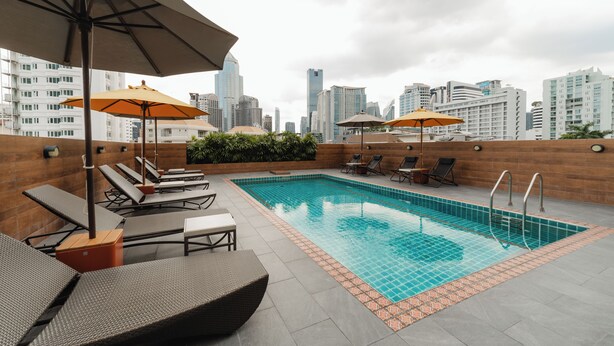 A rooftop pool with lounge chairs and umbrellas, surrounded by a city skyline.