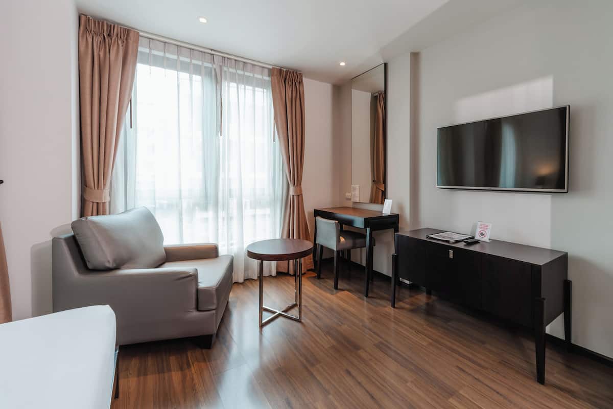 Een moderne hotelkamer met een bank, een klein rond tafeltje, een bureau en een flatscreen televisie aan de muur.