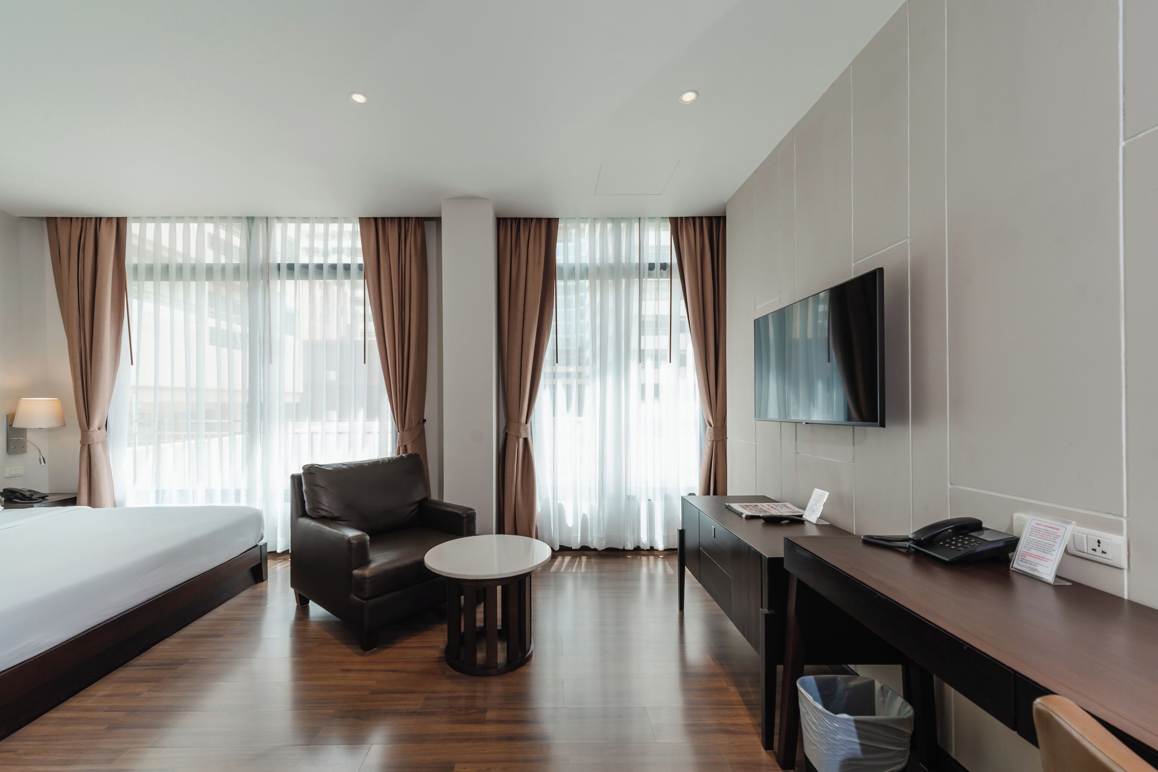 A hotel room with a bed, a desk, a chair, a TV, and a window with curtains.