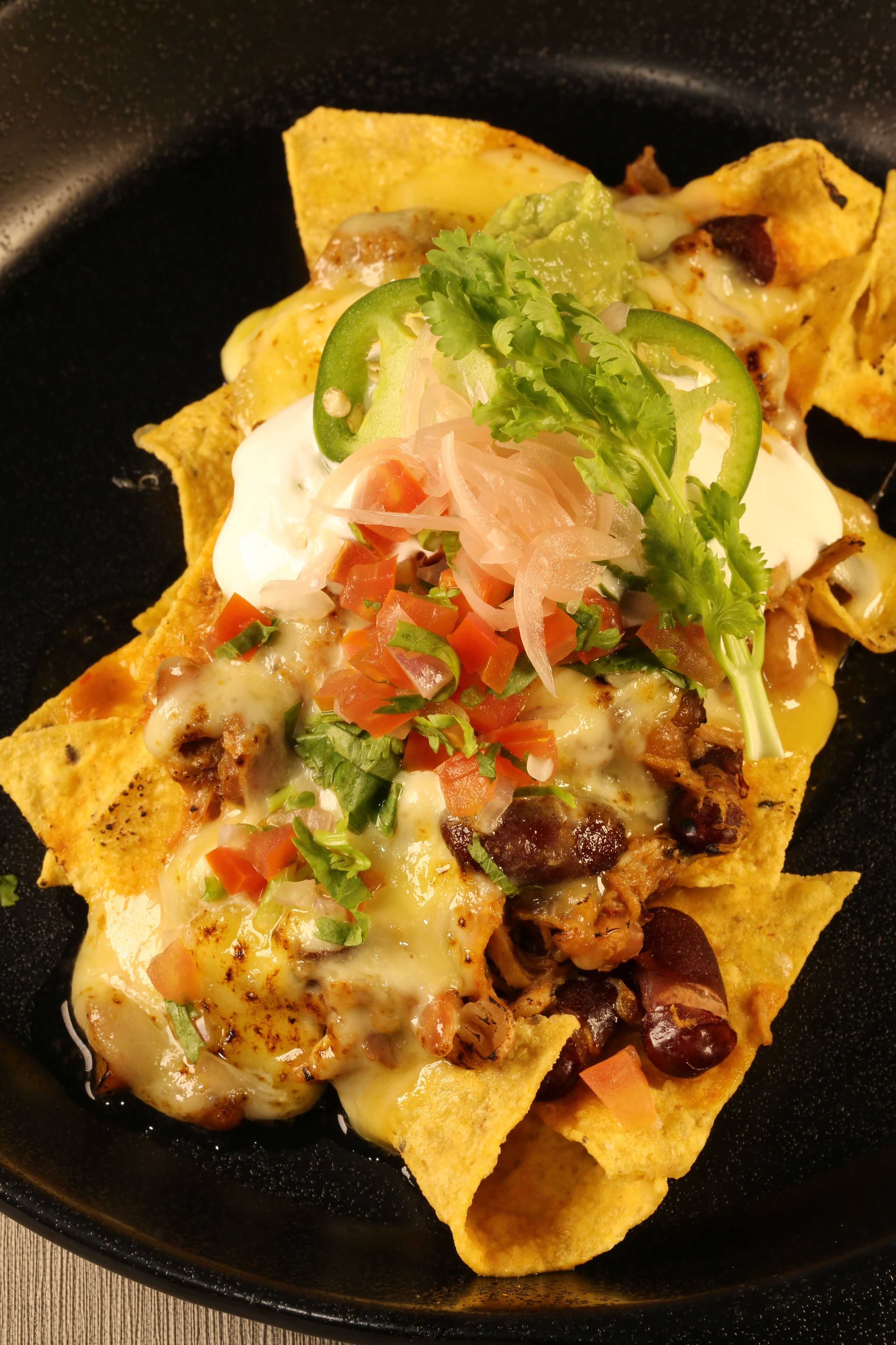 Nachos met gesmolten kaas, jalapeños, tomaten, uien en koriander.
