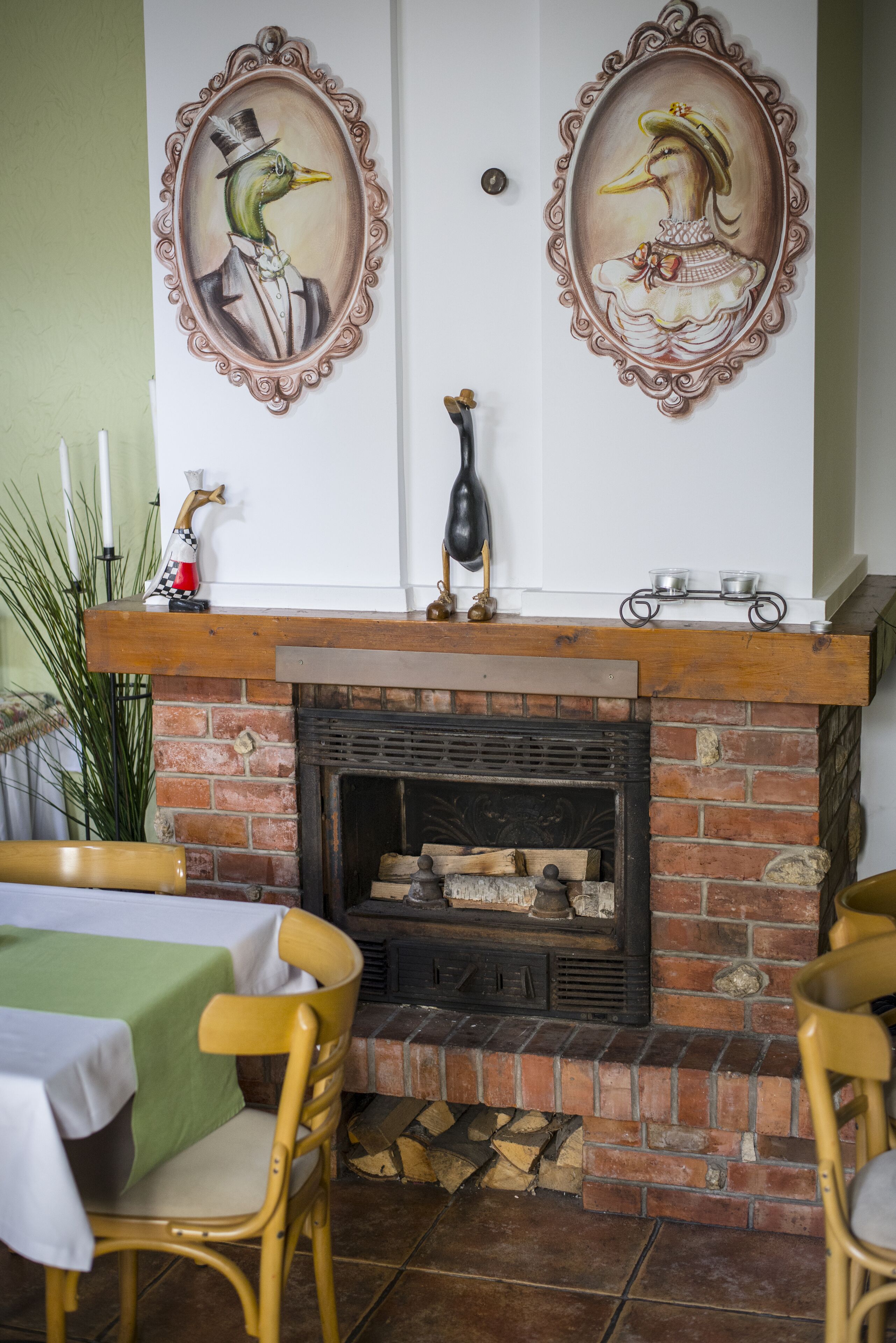 A room with a fireplace, two framed duck paintings, a table with a green tablecloth, and two chairs.