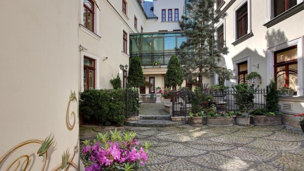 A courtyard with cobblestone flooring, a glass balustrade, and potted plants. - Hotel Wawel (Kraków)