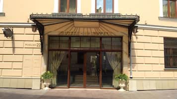 De ingang van Hotel Wawel met een klassiek gevelontwerp, grote glazen deuren en twee potplanten bij de entree.