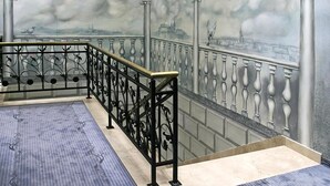 A staircase with ornate black railings and a mural of a bridge with clouds. - Hotel Wawel (Kraków)