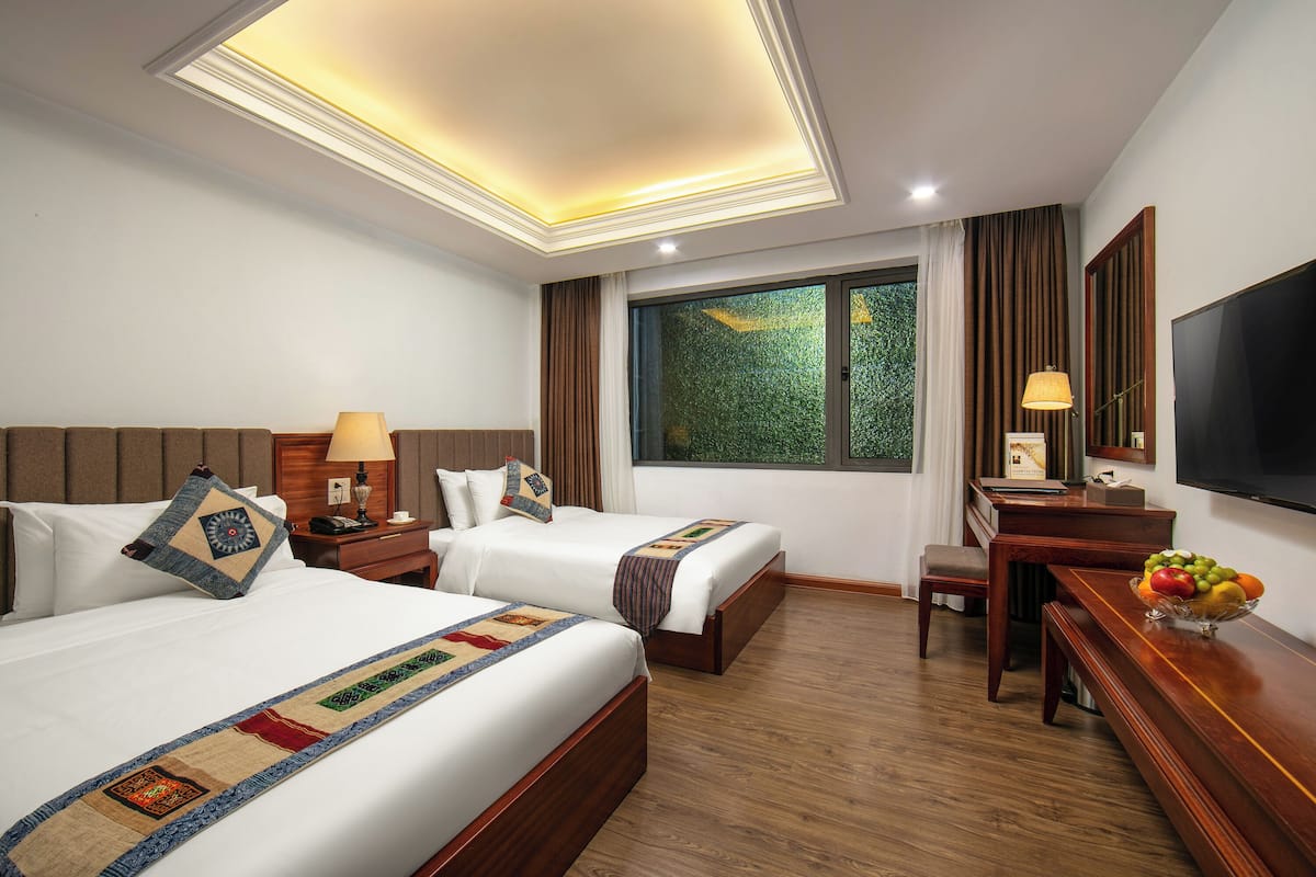 A hotel room with two beds, a desk with a chair, a TV, and a window with curtains.
