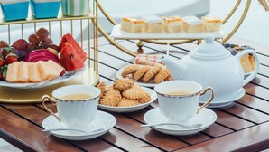 Uma mesa de madeira com um serviço de chá, incluindo bule, xícaras e um suporte escalonado com doces e frutas.