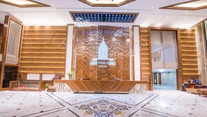Uma área de recepção com design moderno, com balcão de atendimento, parede decorativa com imagem de árvore e edifício, e piso estampado.