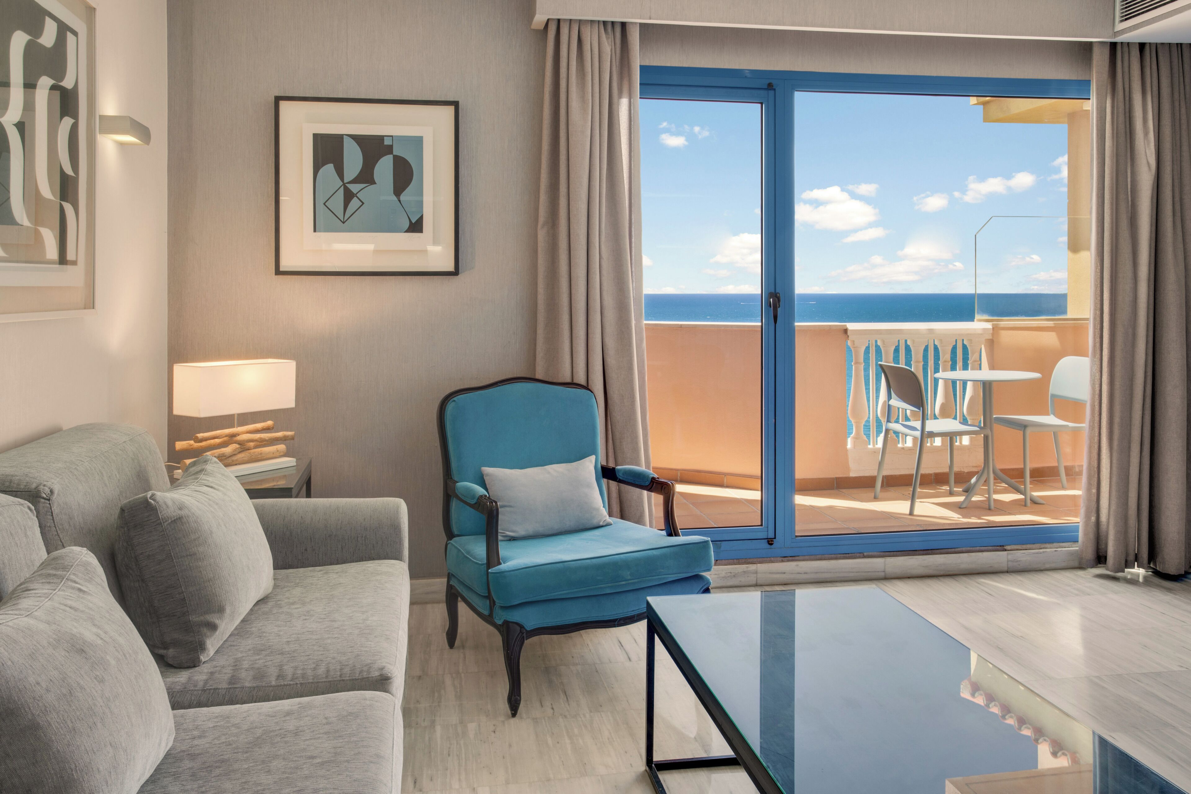 Une chambre d’hôtel avec un balcon, un canapé, une chaise, une table et une lampe.
