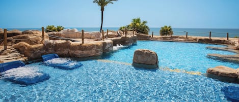 Piscina azul cristalina con formaciones rocosas y palmeras, rodeada por una valla de madera.