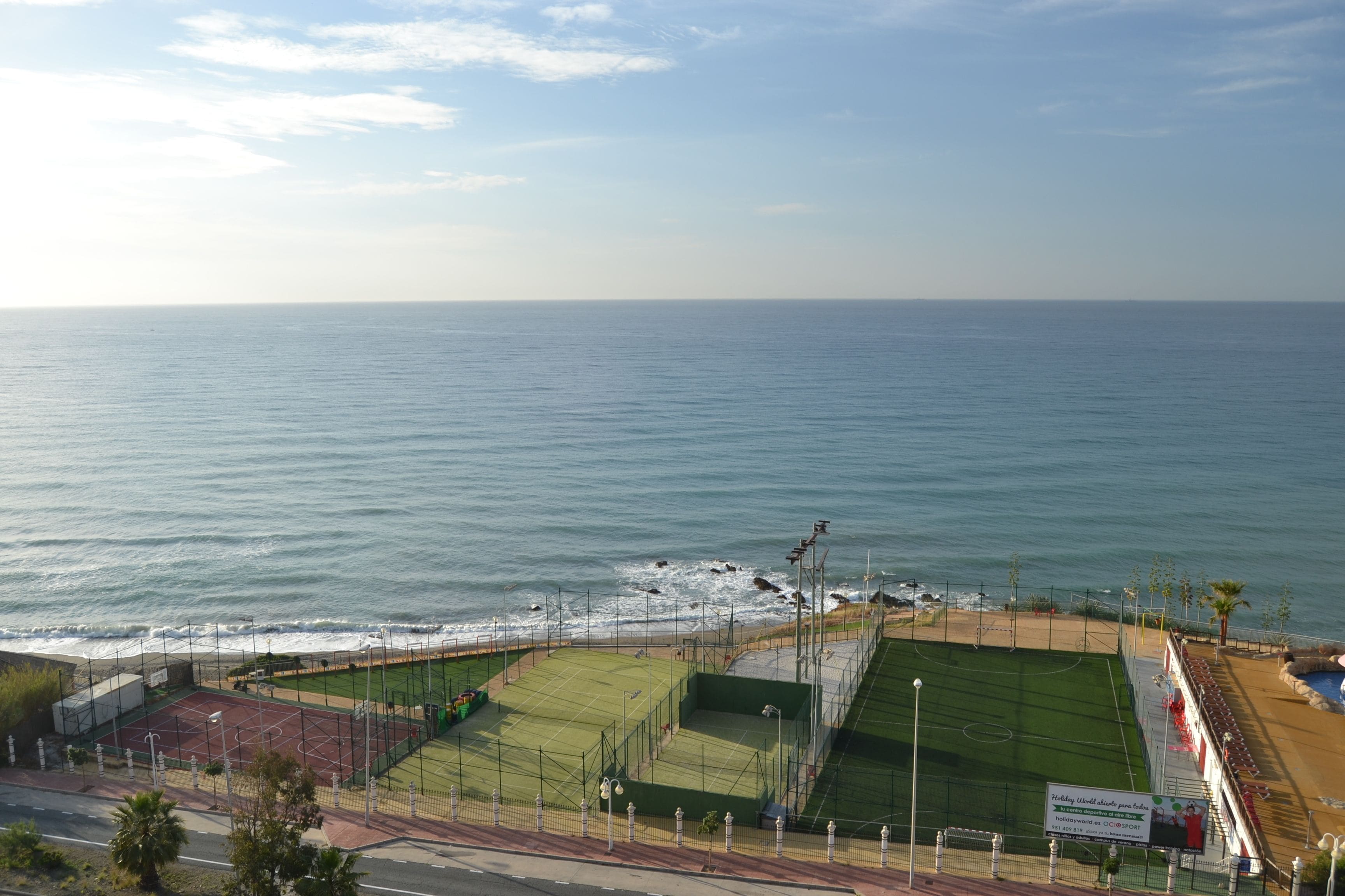 Ein Küsten-Sportkomplex mit mehreren Tennisplätzen, einer Laufbahn und einem Strandabschnitt.