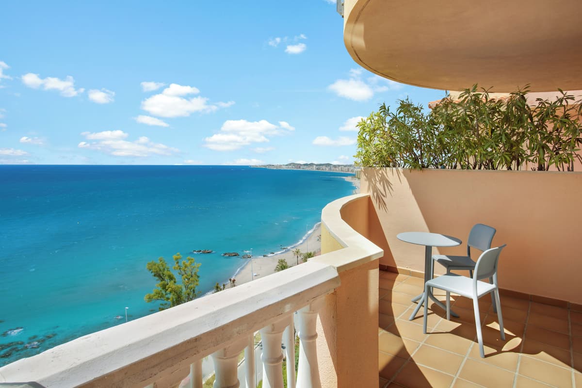 A balcony with a view of the sea, a table with chairs, and potted plants.