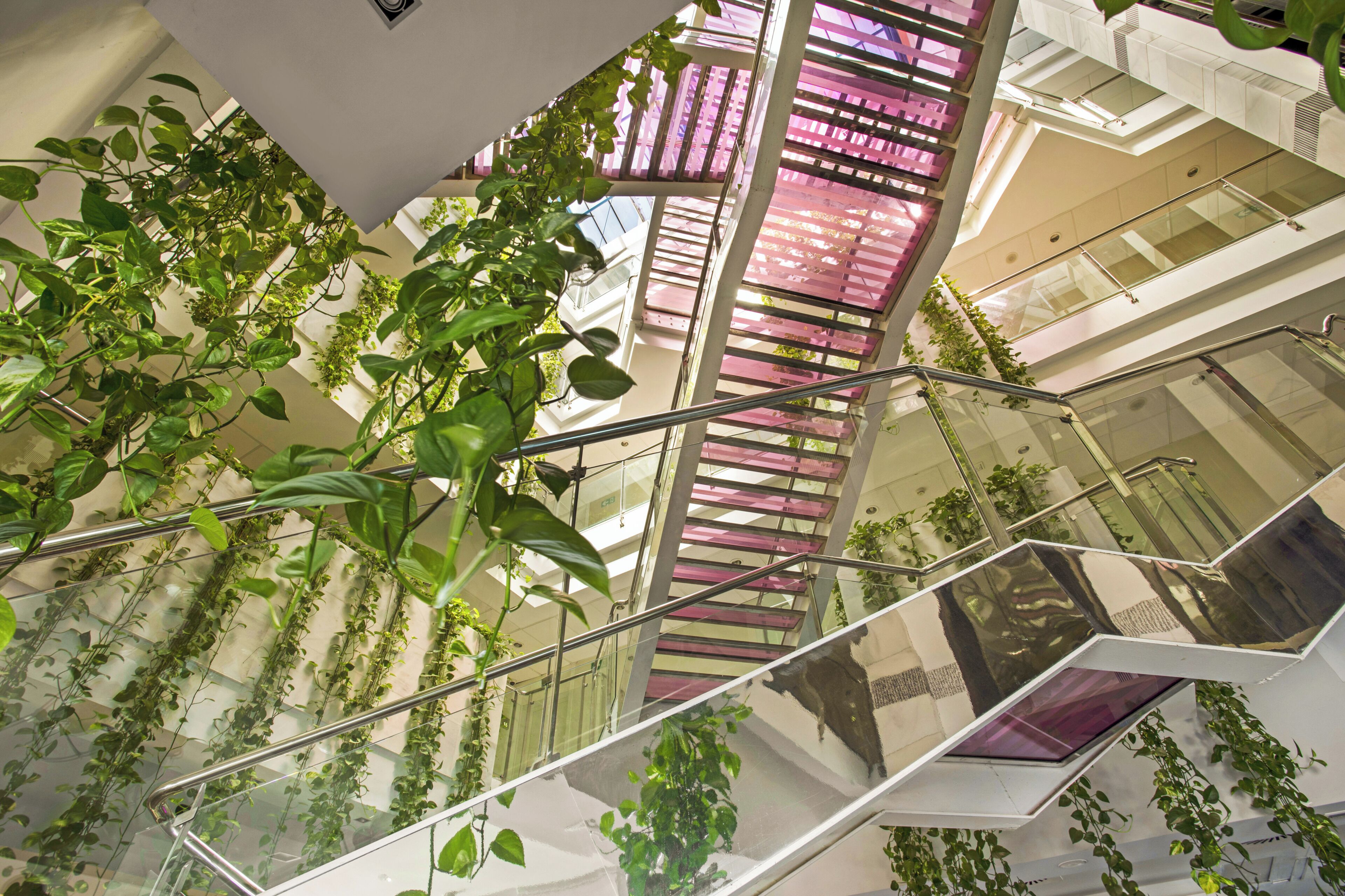 Un interior de varios niveles con barandas de vidrio, plantas y un diseño arquitectónico moderno.