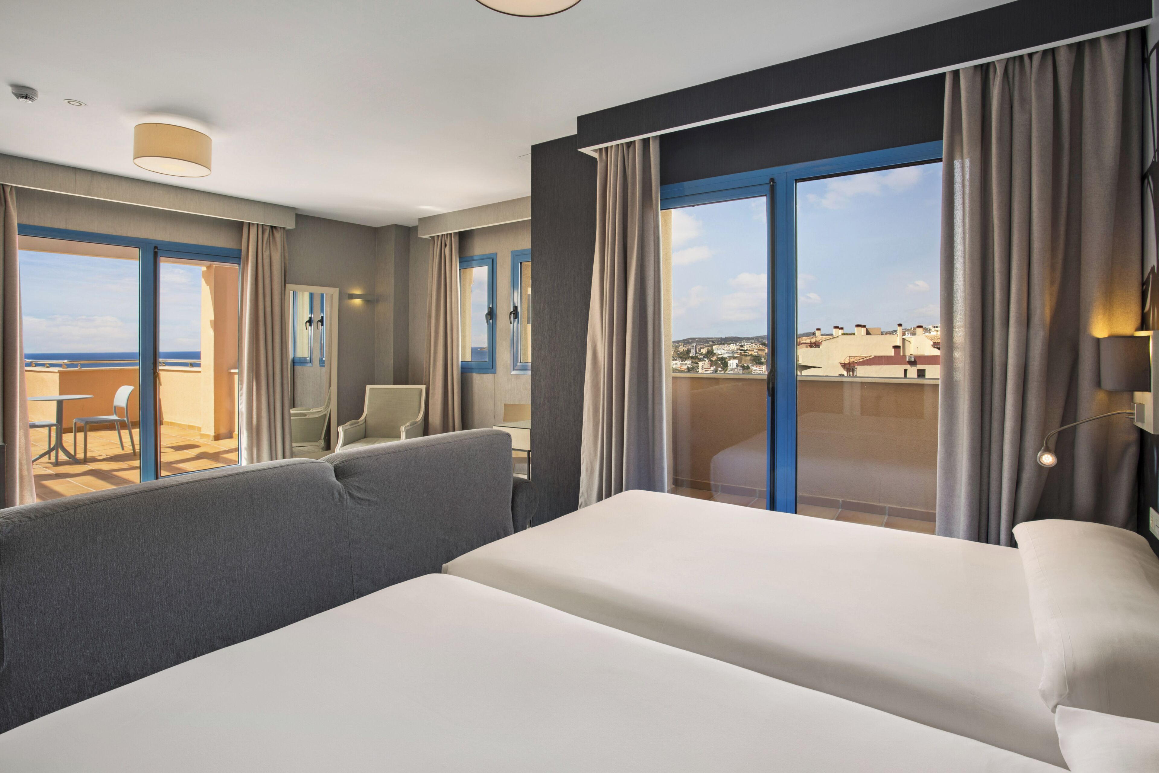Una habitación de hotel con cama, balcón con vistas, zona de estar y una puerta.