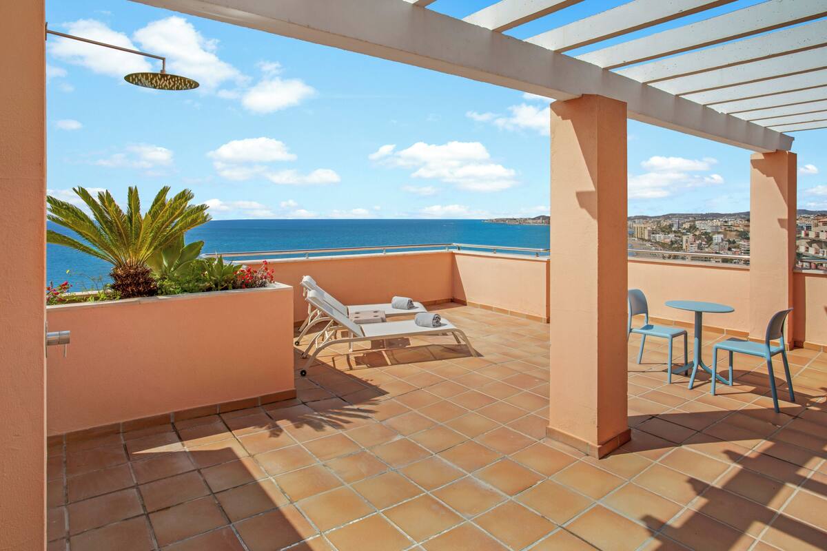 A balcony with a view of the sea, a pergola, and two lounge chairs.