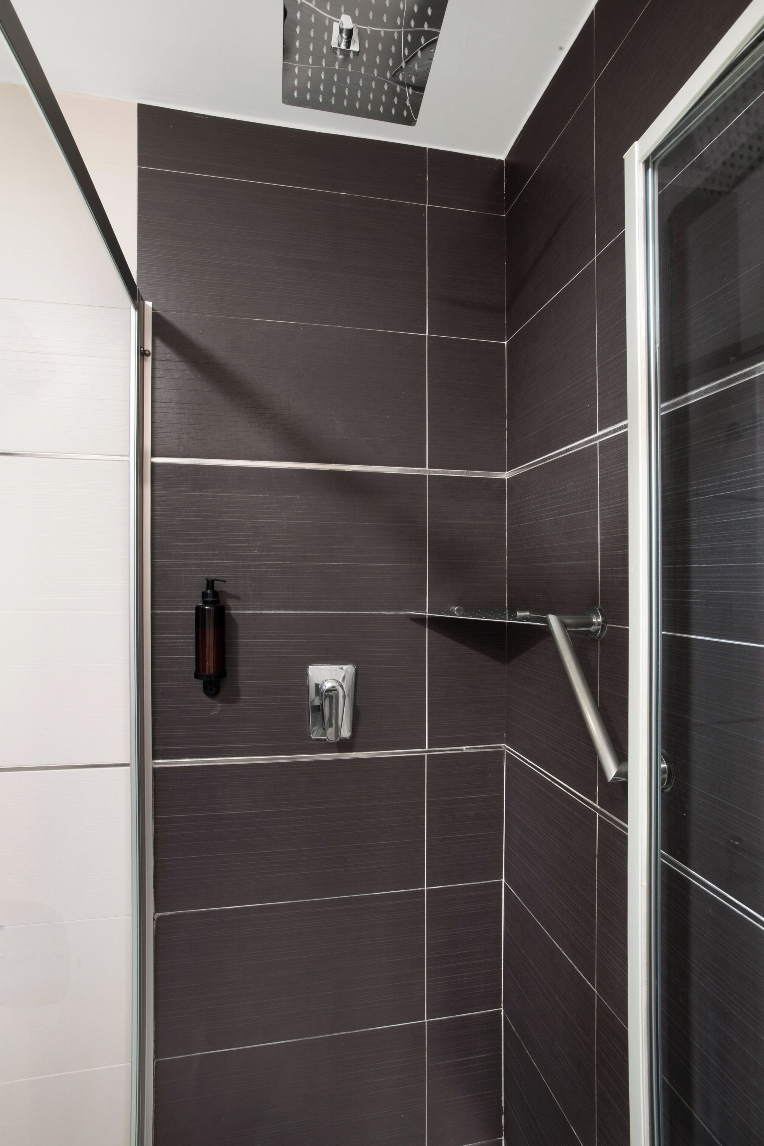 Eine moderne Dusche mit dunklen Fliesen, einer Glasduschwand und einem Seifenspender.