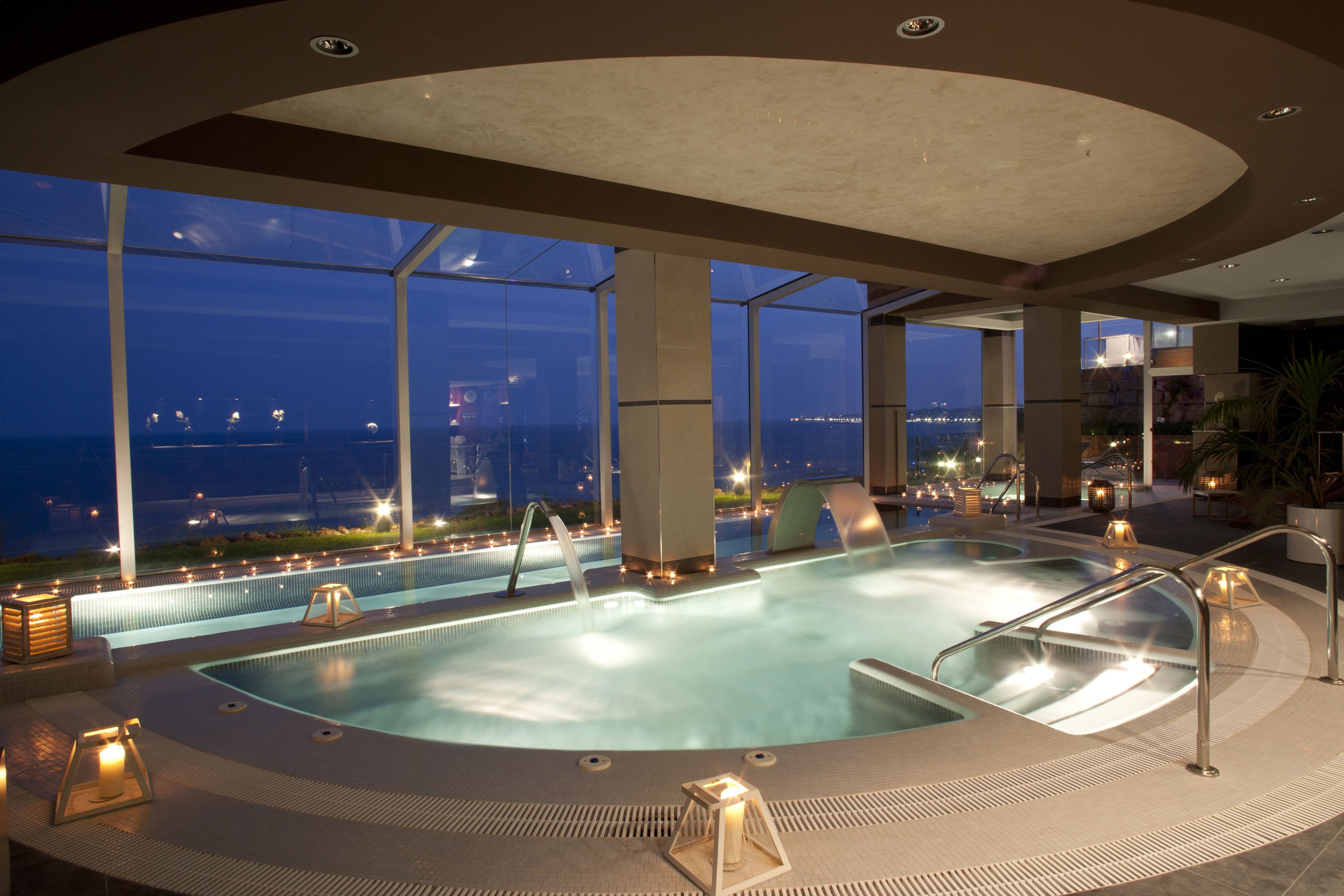 A large indoor swimming pool with a view of the city at dusk.