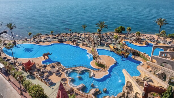 Ein Resort mit mehreren Schwimmbecken, Palmen und Blick auf das Meer.
