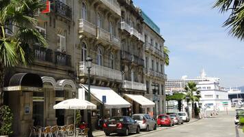 A hotel with a classic facade, outdoor seating, and a view of the sea.