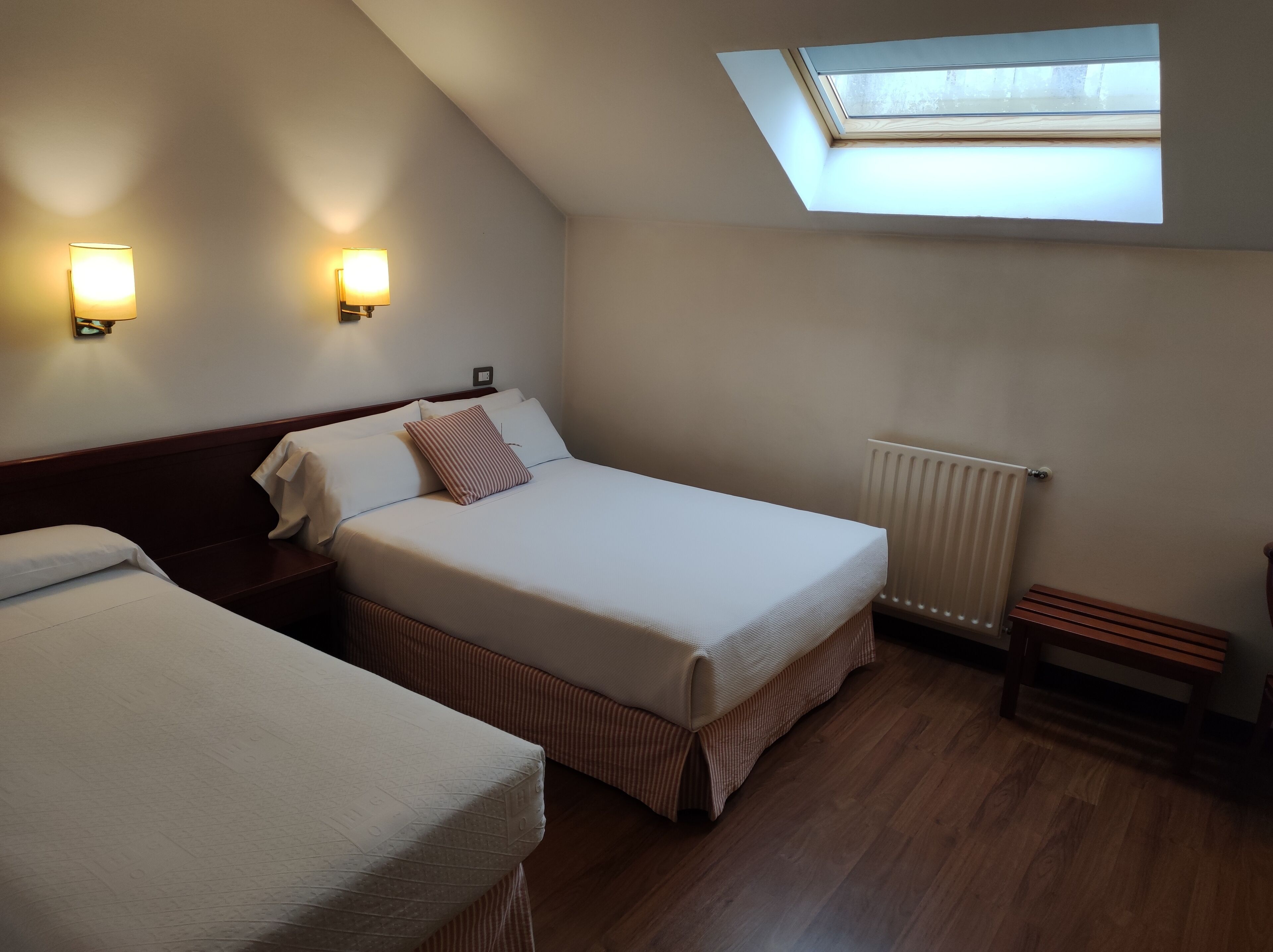 Ein Zimmer mit zwei Betten, einem Oberlicht, einer Heizung und Wandleuchten.