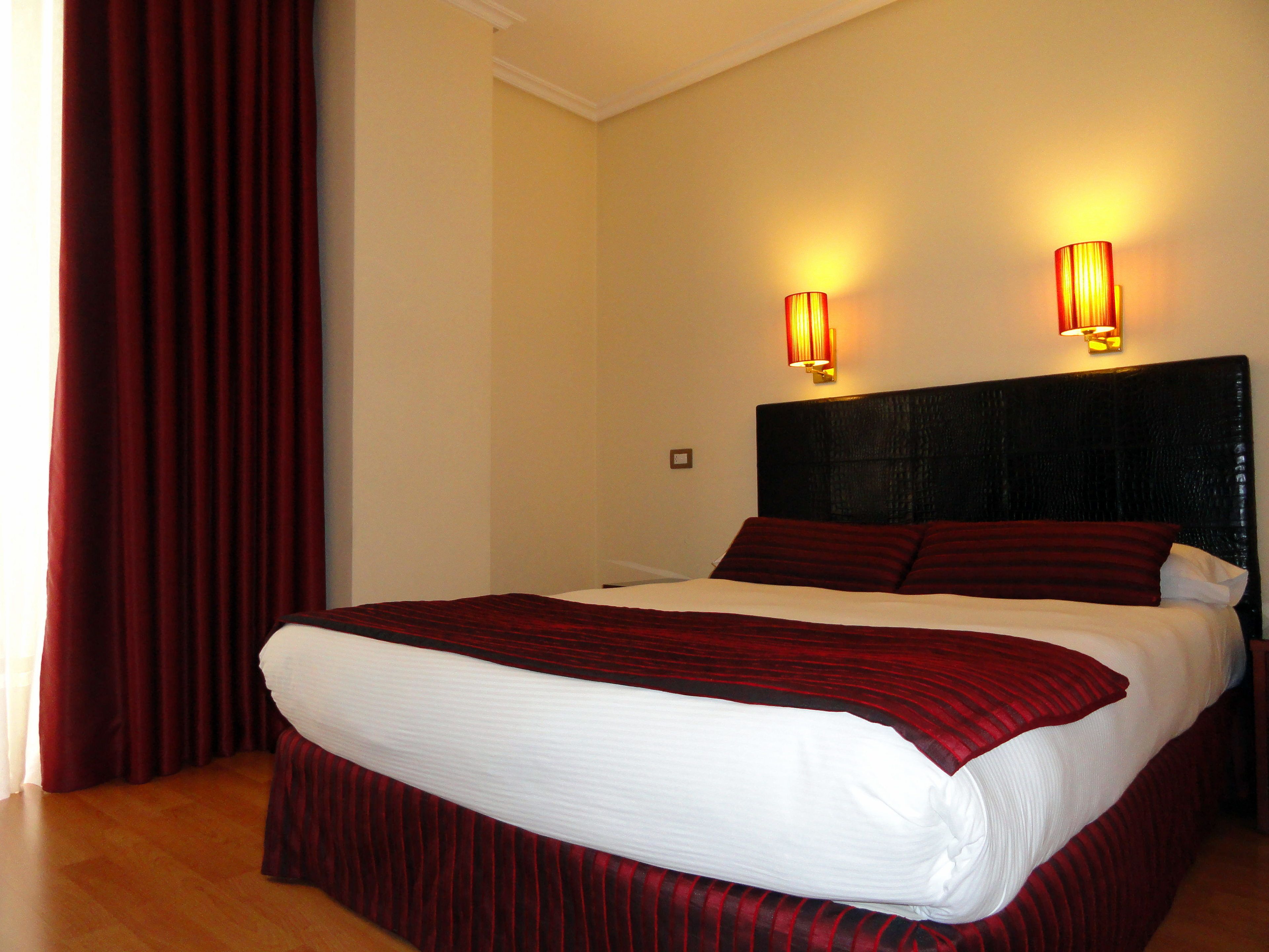 A hotel room with a large bed, two wall-mounted lights, and a red curtain.