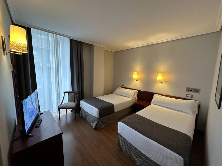 Une chambre d’hôtel avec deux lits, un bureau avec un ordinateur et une chaise.