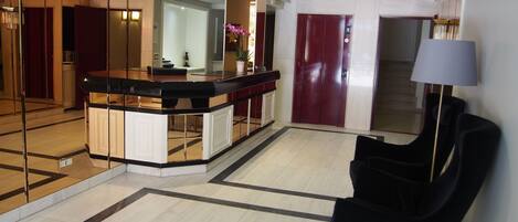 A modern lobby with a reception desk, a staircase, and a black armchair.