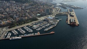 An aerial view of a marina with numerous boats docked, a large building, and a cityscape in the background. - Hotel Compostela Vigo (Vigo)
