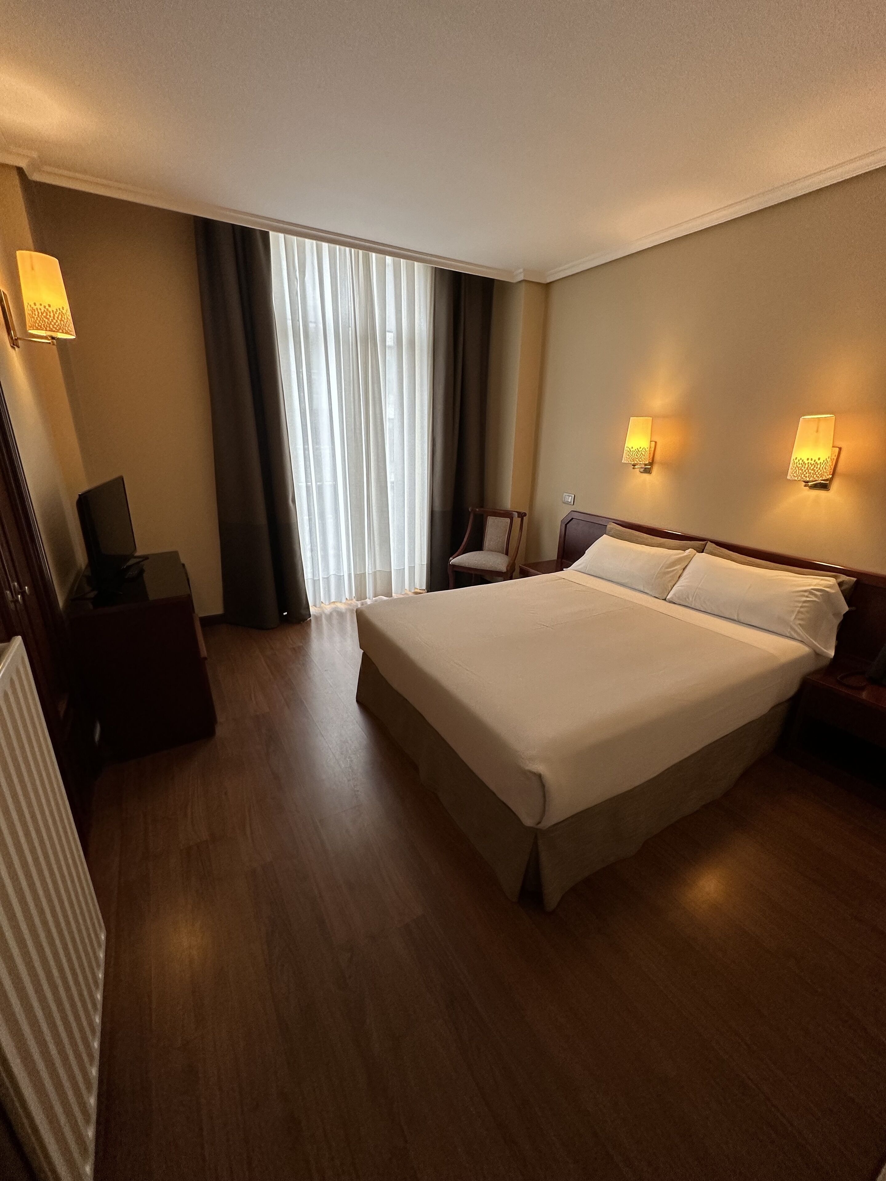 Une chambre d’hôtel avec un grand lit, un bureau, une chaise et deux lampes fixées au mur.