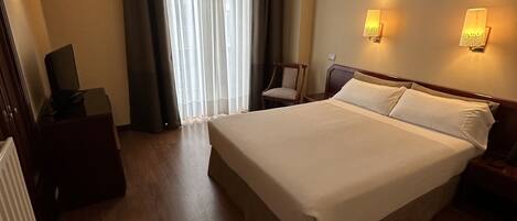 Una habitación de hotel con una cama grande, un escritorio, una silla y dos lámparas fijadas a la pared.